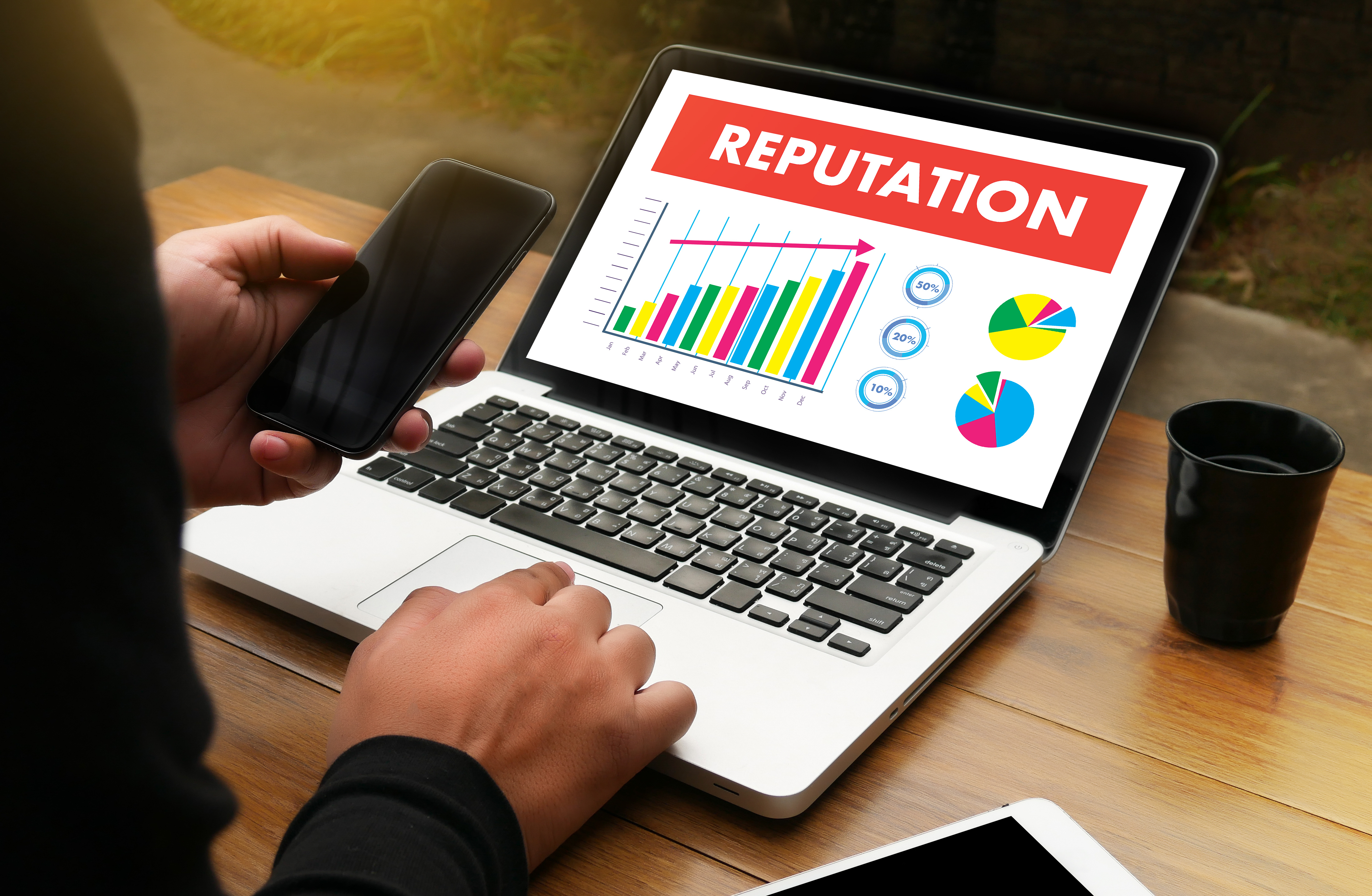 Hands writing on a cellphone and on a computer showing graphs about Online Reputation. 